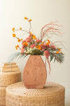 Decorative vase with flowers on a woven stool against a plain background