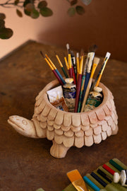 Tortoise-shaped ceramic holder with art supplies on a wooden surface