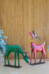 Two metal reindeer sculptures, one green and one red, against a wooden paneled wall.