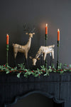 Decorative mantel with deer figurines, candles, and greenery against a dark background