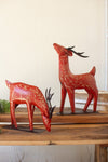 Two red deer figurines with gold patterns on a wooden surface.