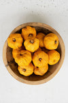 Wooden bowl filled with yellow gourds on a white surface