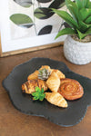 Assorted pastries on a black plate with a plant and framed picture in the background.