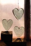Three heart-shaped glass ornaments hanging against a neutral background