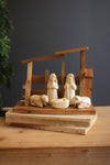 Wooden nativity scene with figures and stable on a wooden base against a dark background.