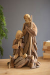 Wooden nativity scene figurines on a wooden surface with a gray background