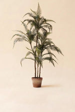 An artificial palm tree with green fronds in a brown pot, centered against a solid beige background.