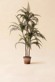 An artificial palm tree with green fronds in a brown pot, centered against a solid beige background.