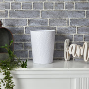 White textured trash can on a white surface with a brick wall background