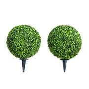 Two artificial topiary balls on stands against a white background