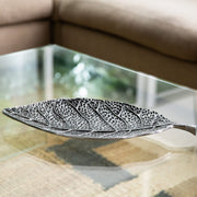 Decorative leaf-shaped silver platter on a glass table