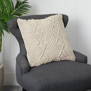 Textured beige pillow on a gray armchair with a plant in the background