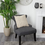 Gray chair with a textured pillow in a room with a plant and fireplace.