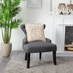 Gray armchair with a textured pillow in a room with a plant and fireplace.