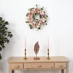 Floral wreath on a white wall above a wooden table with candles and a decorative feather.