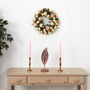 Decorative wreath with flowers on a white wall above a wooden table with candles and a leaf sculpture.