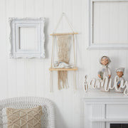 Decorative wall setup with a macrame hanging, framed picture, and decorative items on a white wall.