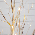 A decorative artificial tree with slender branches wrapped in white faux bark and illuminated by small warm white fairy lights, shown against a light gray paneled background.