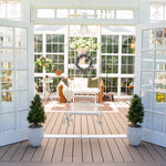 Sunroom with wooden floor, white walls, and large windows, featuring a wicker chair and potted plants.