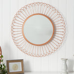 Decorative round mirror with a gold wire frame on a white wall.