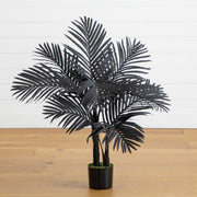 Black artificial palm plant in a pot on a wooden floor with a white wall background