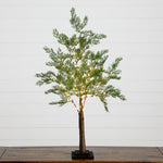 A small artificial Christmas tree with green pine-like foliage, warm white string lights, a brown trunk, and a black square base, displayed on a wooden surface against a white paneled wall.