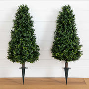 Two artificial topiary trees on stands against a white wooden panel background