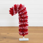 A red and white frosted tinsel candy cane Christmas tree decoration on a white display stand, set against a white paneled wall and light wood floor.