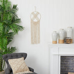 Living room with a gray armchair, decorative pillow, macrame wall hanging, and white vases.
