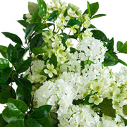 White faux hydrangea and small white blossoms with glossy green leaves, photographed against a plain white background.