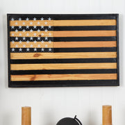 Wooden American flag wall art on a white wall with candles and a helmet in the background.