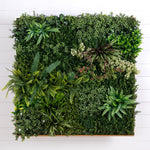 A square artificial green wall arrangement made of many different leafy plants and ferns, photographed from above against a white shiplap wall.