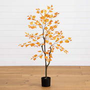 Artificial tree with orange leaves in a pot on a wooden floor against a white wall.