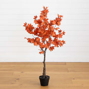 Potted artificial tree with orange leaves on a wooden floor and white wall background