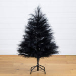 Black artificial Christmas tree on a wooden floor with a white wall background