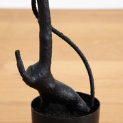 Black metal sculpture of a bear hanging from a branch in a pot on a wooden surface