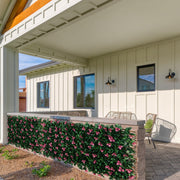 A long decorative planter wall covered in dense green foliage and pink flowers, installed along a covered patio in front of a house with cream siding and dark windows.