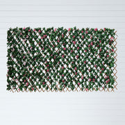 A rectangular artificial greenery wall panel featuring dense green faux leaves, pink faux flowers, and a brown lattice trellis frame, displayed against a white background with horizontal lines.