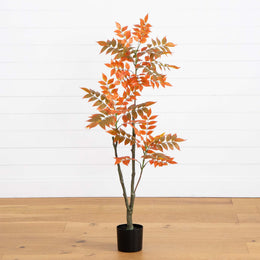Artificial potted plant with orange leaves on a wooden floor and white wall background