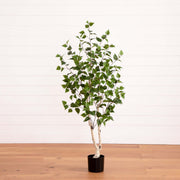 Potted artificial tree with green leaves on a wooden floor and white wall background