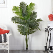 Artificial palm plant in a living room setting with a white wall and decorative items.