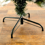 A close-up of a black metal Christmas tree stand supporting a green artificial tree, set on a brown wooden floor.