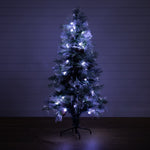 A pre-lit artificial Christmas tree with a white frosted finish, decorated with glowing white lights, standing on a black metal stand against a dark paneled wall.