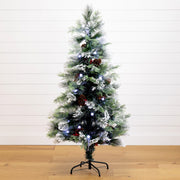 A pre-lit artificial Christmas tree with a white frosted finish, decorated with pinecones, ornaments, and blue lights, standing on a black metal stand against a white shiplap wall and light wood floor.