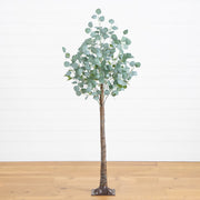 An artificial eucalyptus tree with a realistic brown trunk and round silver-green leaves, standing on a wooden floor against a white paneled wall.