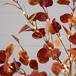 Decorative string lights on a branch with red leaves against a light background