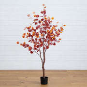 Artificial potted tree with red and orange leaves on a wooden floor with a white wall background