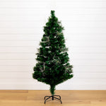 A green artificial Christmas tree with white tinsel garland, standing on a black metal stand against a white shiplap wall and light wood floor.