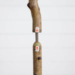 A close-up of a wooden walking cane with a textured natural wood handle and shaft, featuring a metal connector and two small white stickers with red arrows and numbers.