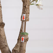 A close-up of a tree trunk with two small white tags attached, one with a red downward arrow labeled 'L' and the other with a red upward arrow labeled '1'.